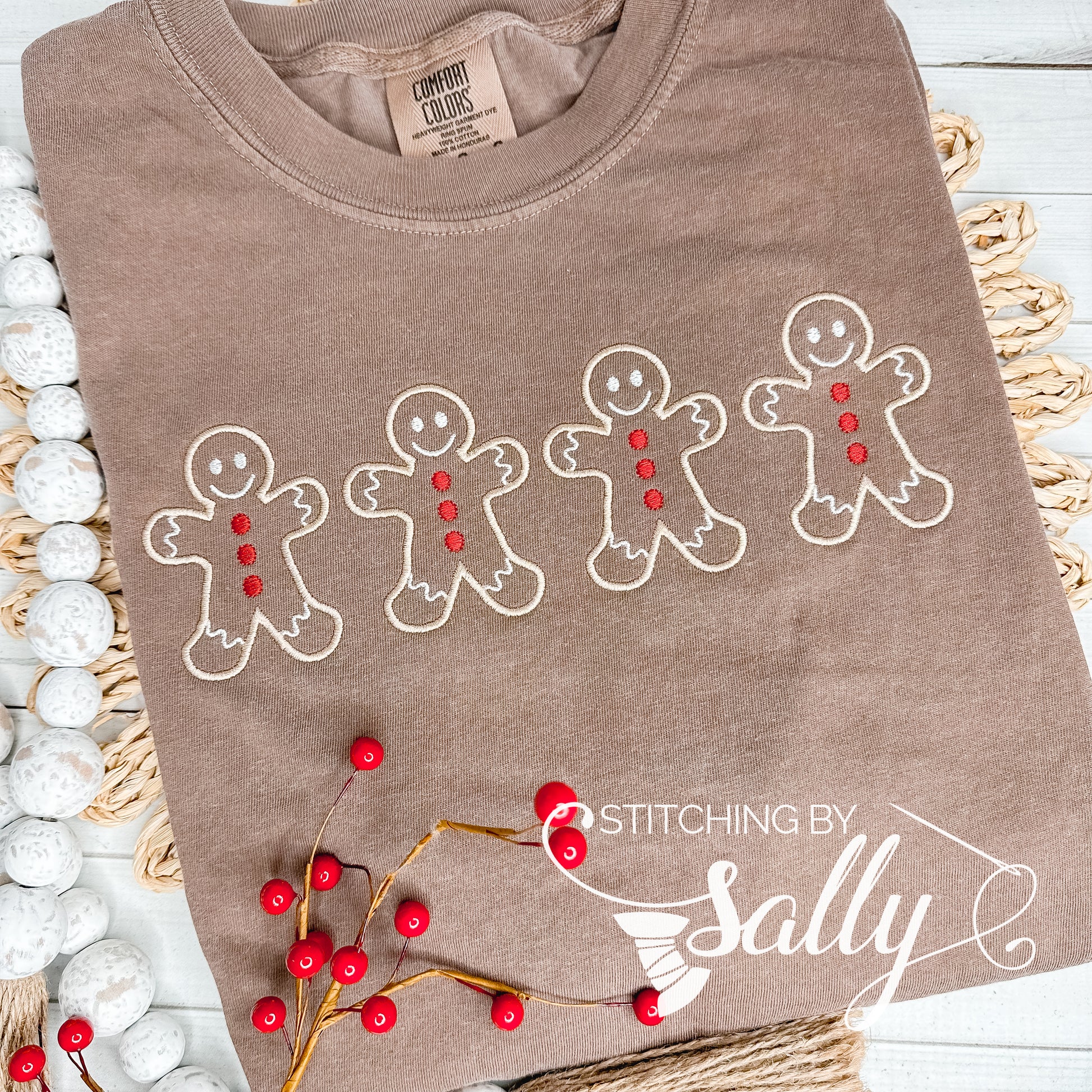 A brown shirt with four Gingerbread men embroidered in tan thread with red buttons. Stitching by Sally 