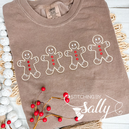 A brown shirt with four Gingerbread men embroidered in tan thread with red buttons. Stitching by Sally 