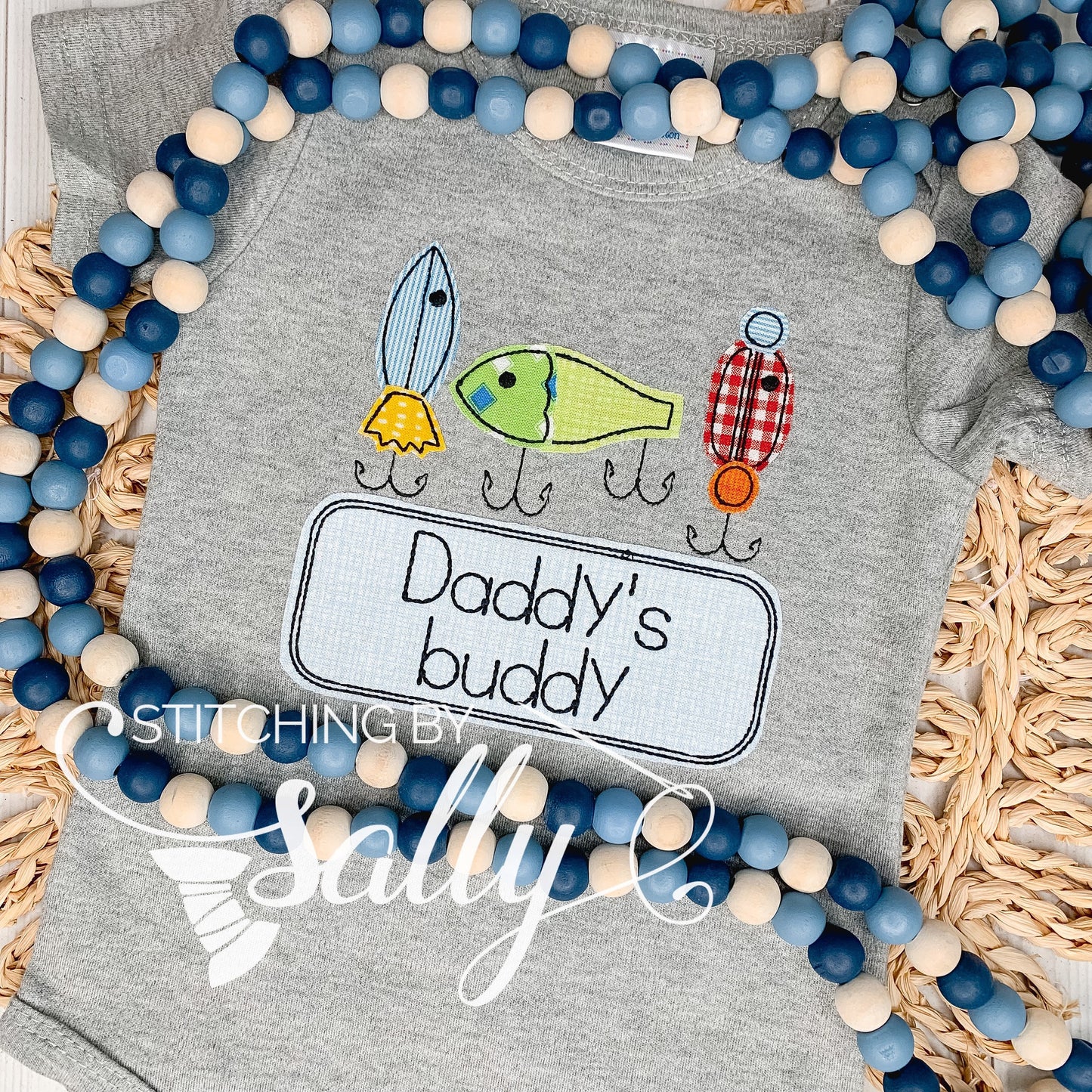 A grey shirt with 3 fishing lures appliquéd in cute fabric. Daddy's buddy is embroidered underneath.