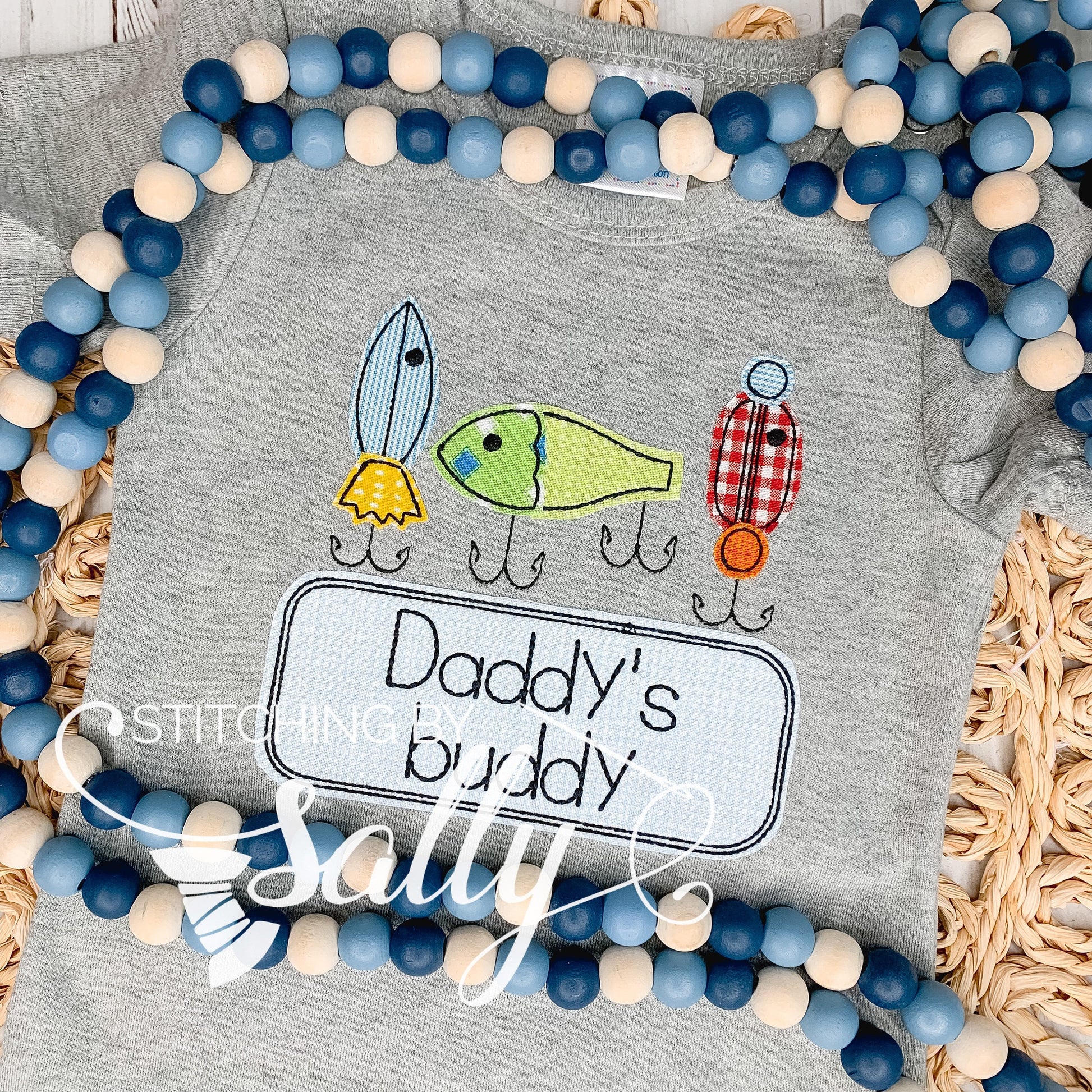 A grey shirt with 3 fishing lures appliquéd in cute fabric. Daddy's buddy is embroidered underneath.