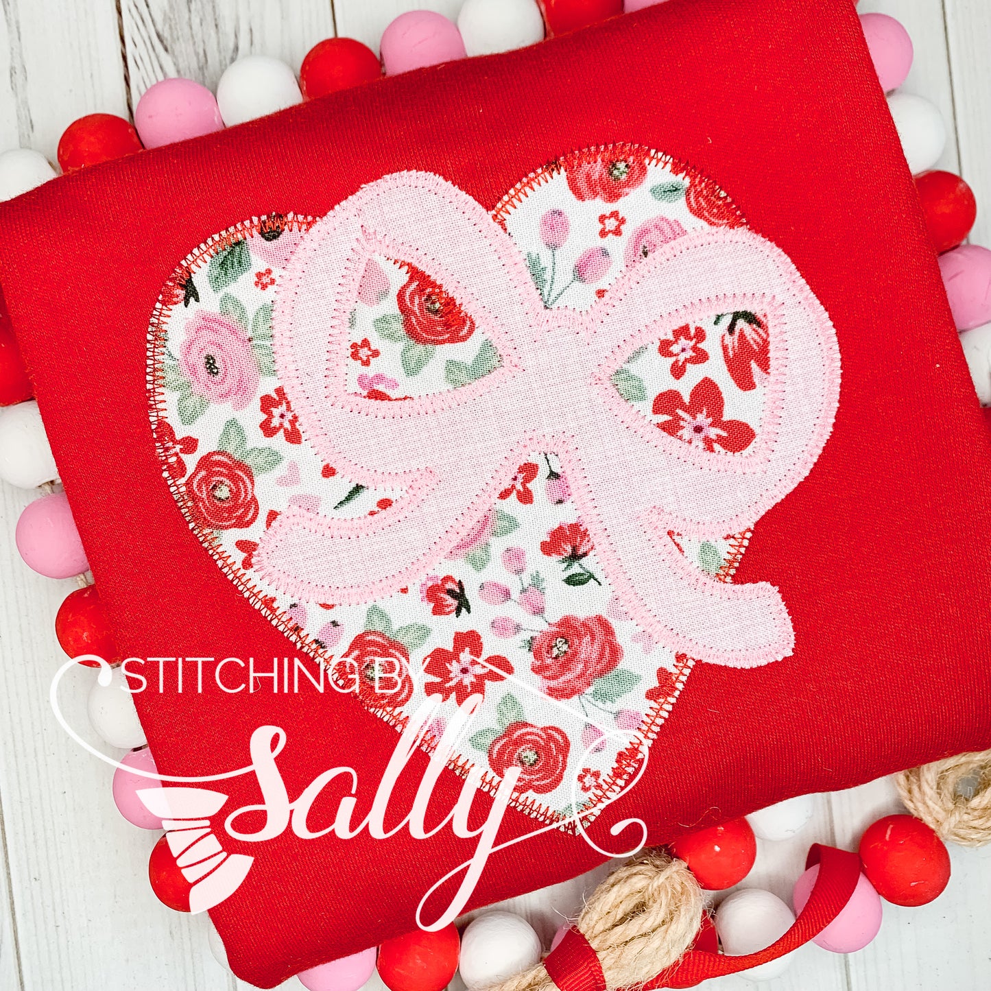 A red shirt with a heart appliqué with pink and red rose fabric. A cute pink bow is appliqués on the heart. 