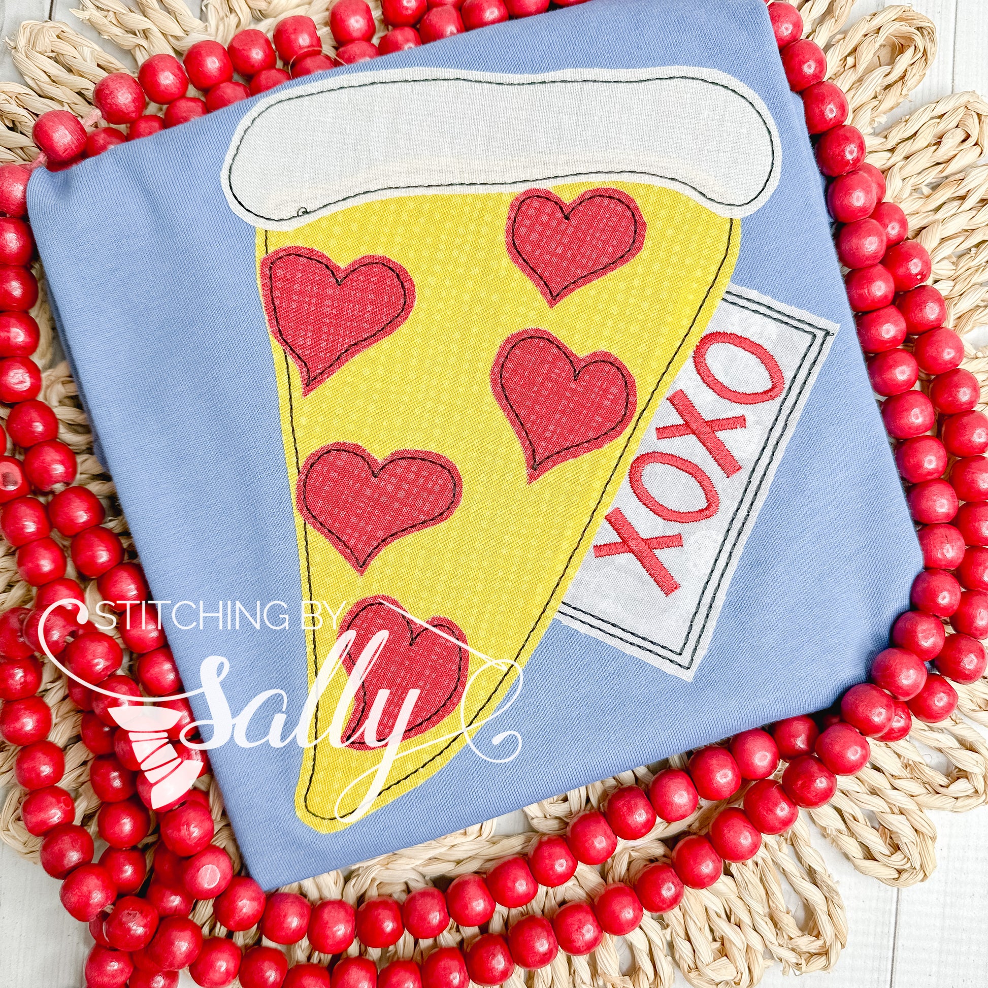 A blue shirt with love pizza appliqué design. Xoxo is embroidered in red thread. 