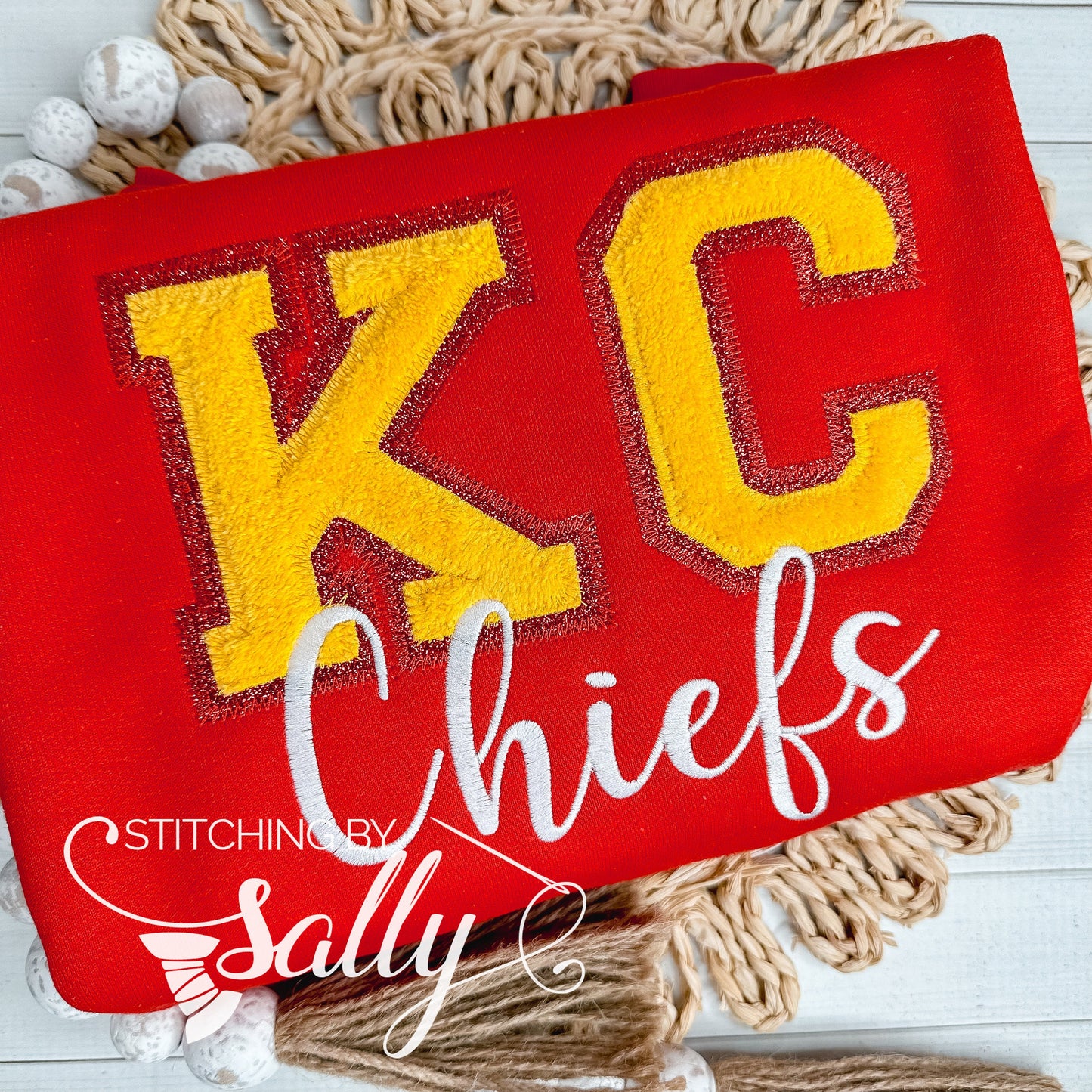 A red youth crewneck with faux chenille KC letters in yellow and red with white Chiefs embroidered underneath.