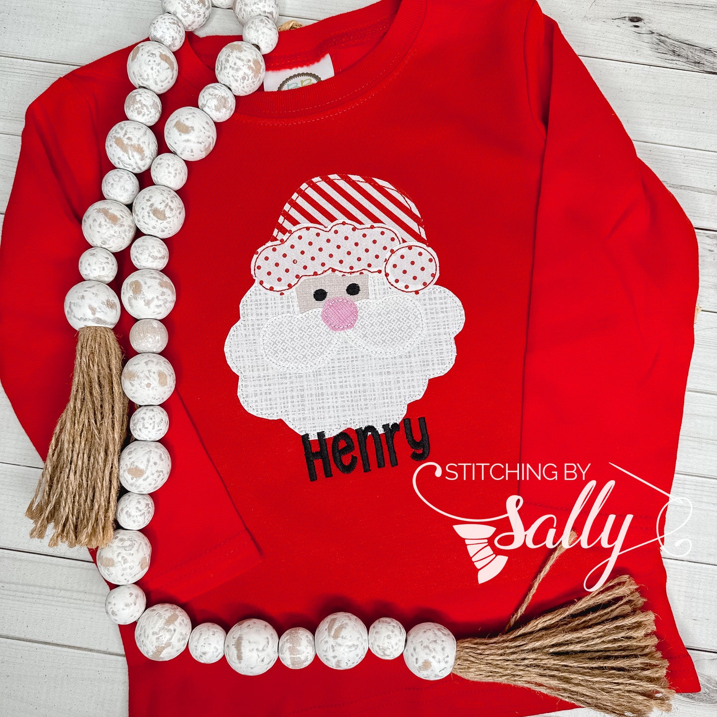 A red shirt with a santa face applique in red and white fabric. Personalized with name in black thread. 