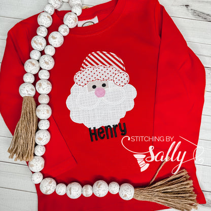 A red shirt with a santa face applique in red and white fabric. Personalized with name in black thread. 