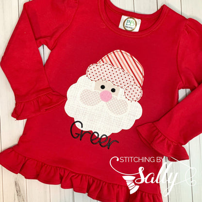 A long sleeve red shirt with ruffles with a santa face applique in red and white fabric. Personalized with name in black thread. 