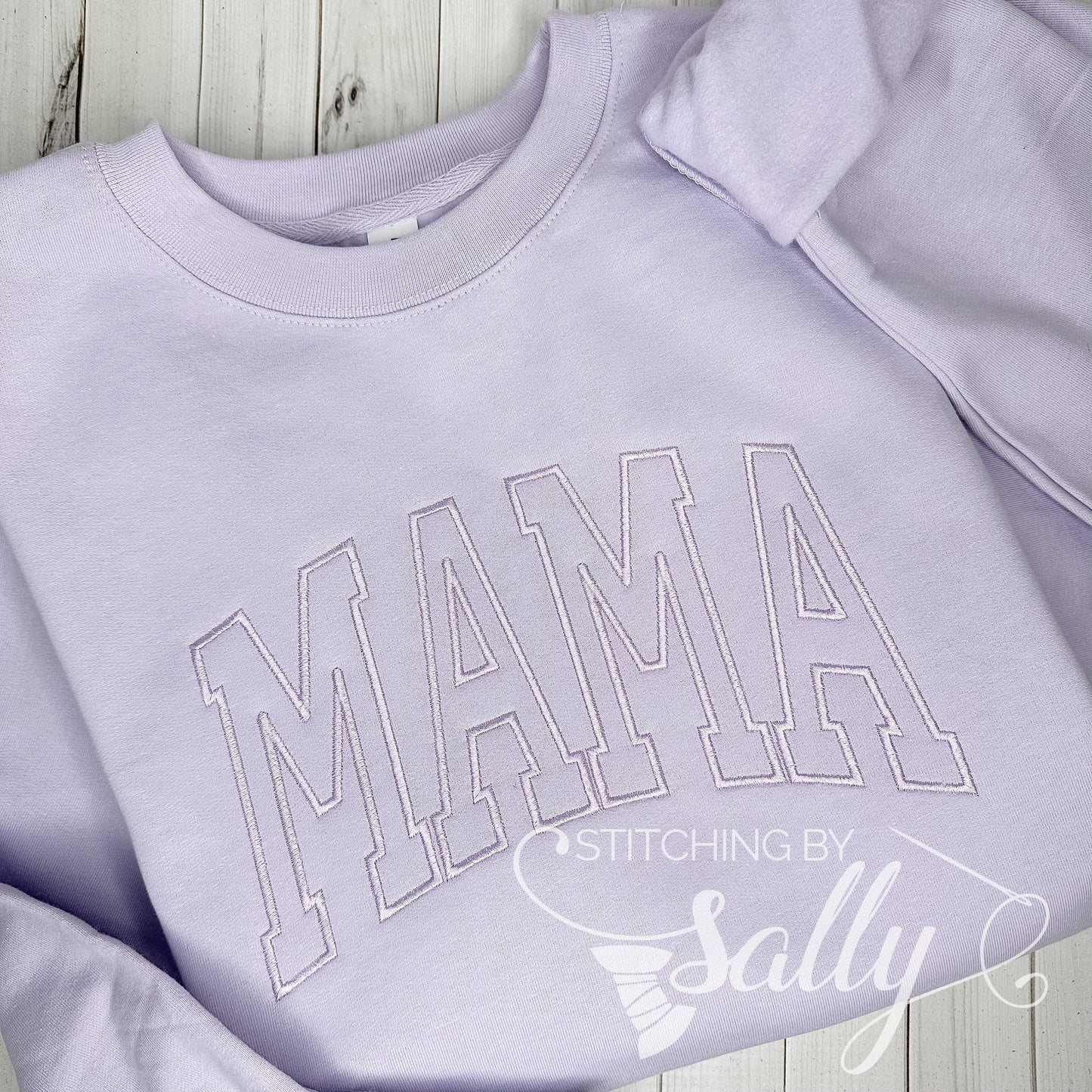 A lavender crewneck embroidered with MAMA in a varsity font in a light purple thread for a timeless tone on tone, minimalistic look.