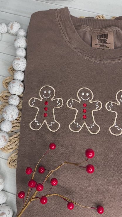 A video of a brown shirt with four Gingerbread men embroidered in tan thread with red buttons. Stitching by Sally 